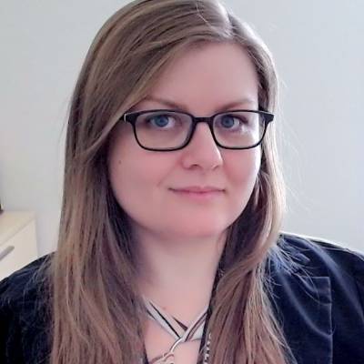 A caucasian female with long blonde hair and glasses facing the camera. 