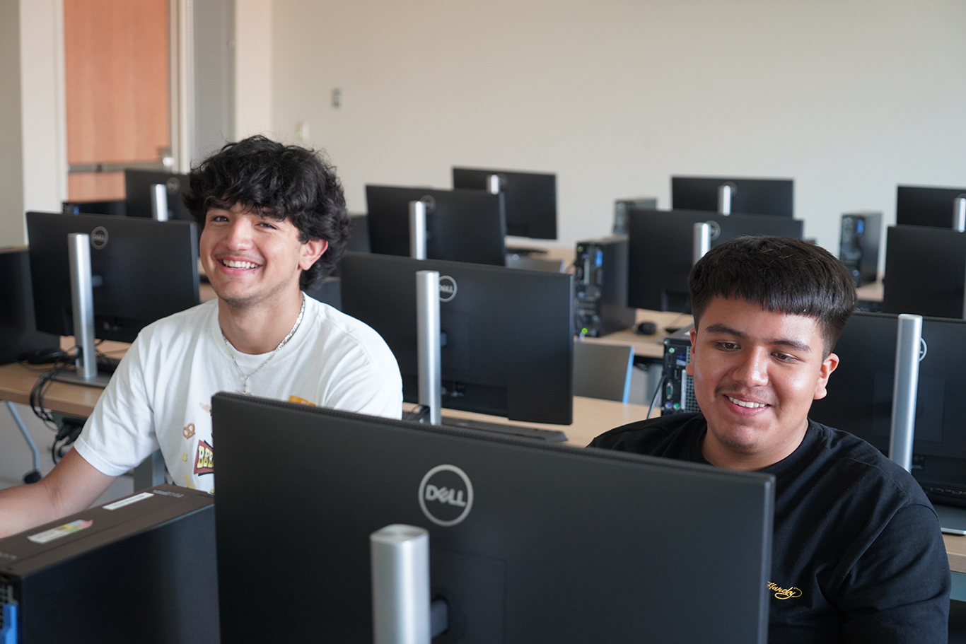 Students smiling in front of computers