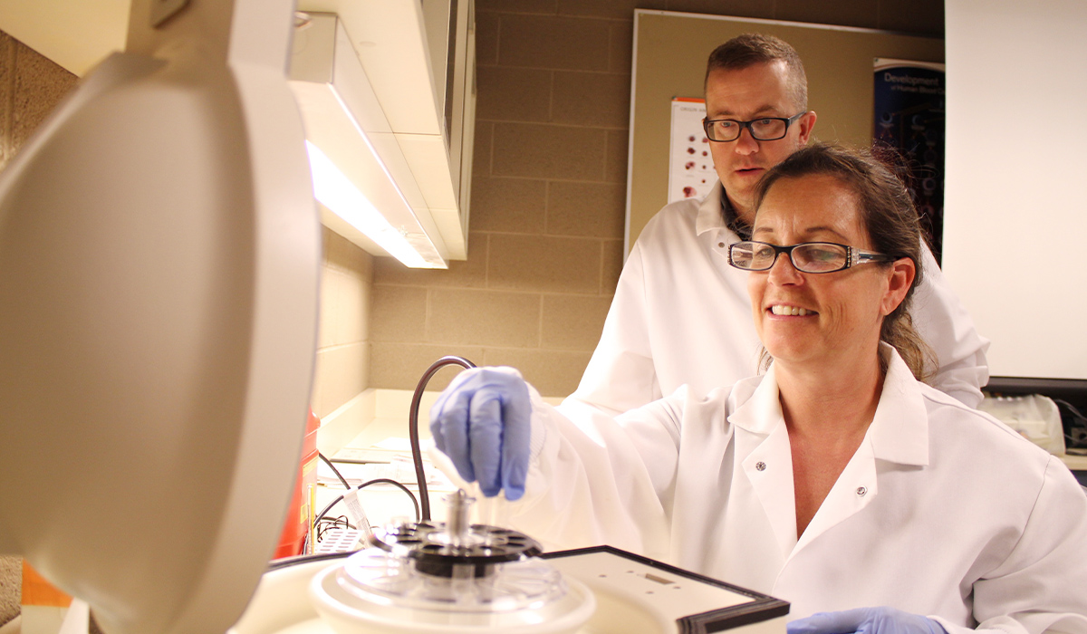 A medical assistant student works with a microscope while the professor observes.