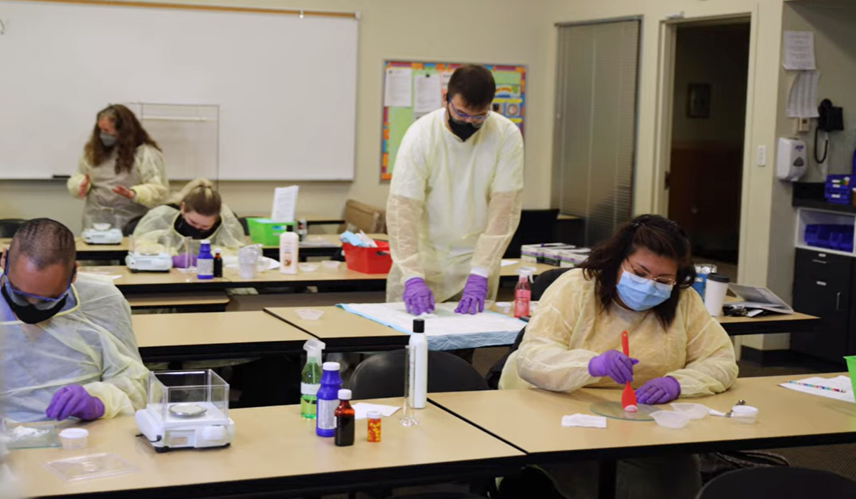 Pharmacy technician students sit at tables to complete a lab project.