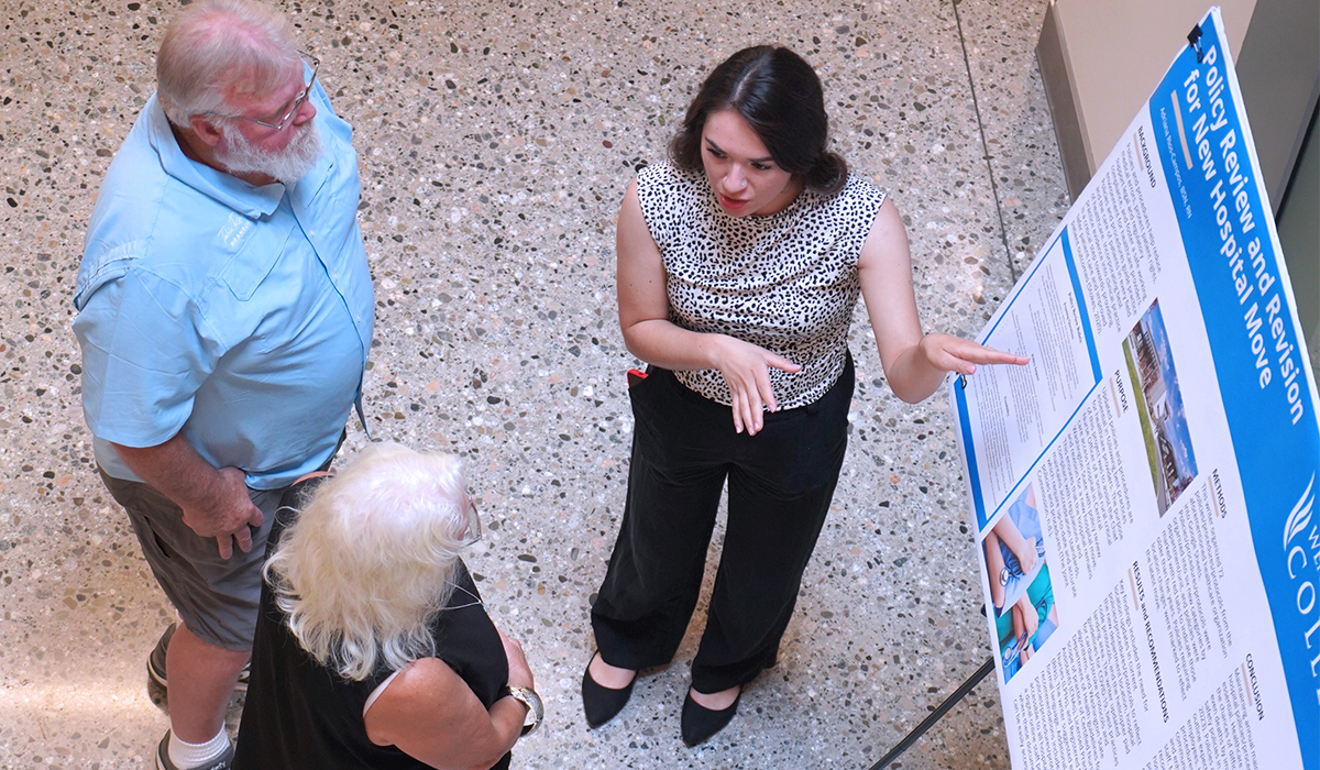 An overhead view of an RN to BSN graduate explaining her poster project to visitors.