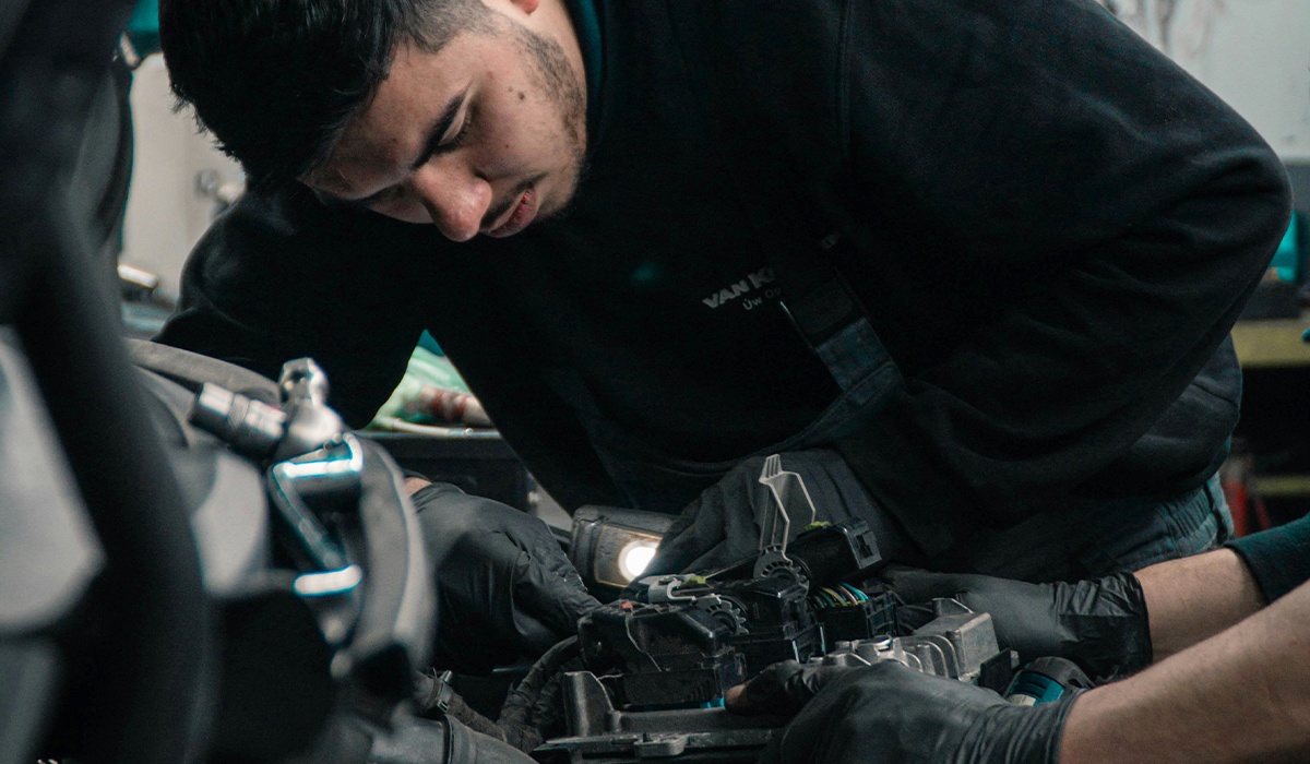 A pair of mechanics work on wiring inside a car's engine.