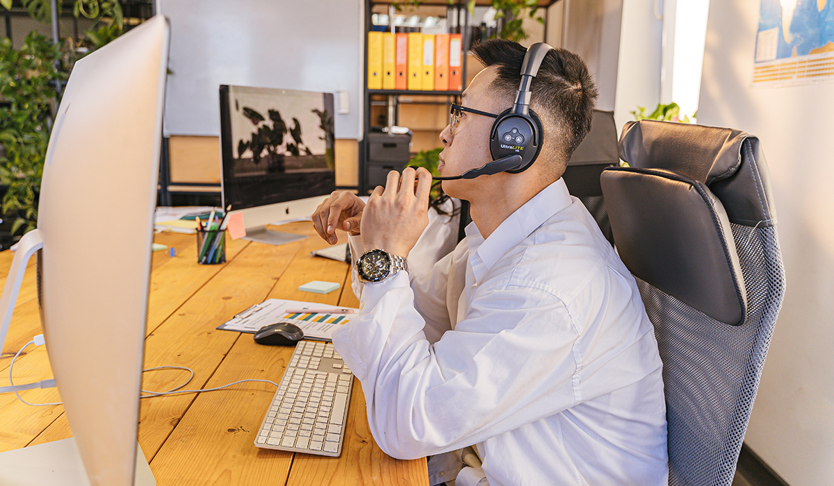 A person wearing a headset sits at a desk and observes two computer monitors.