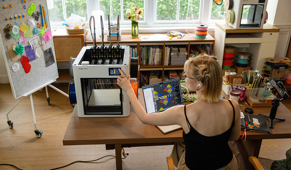 A designer sits at a desk and works on a 3D printer.