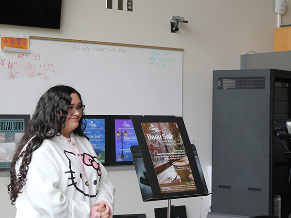 A graphic design student stands next to a poster that she created.