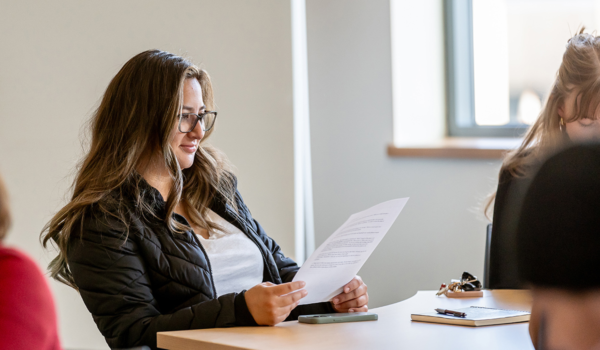 A student sits at a desk and reads a paper.