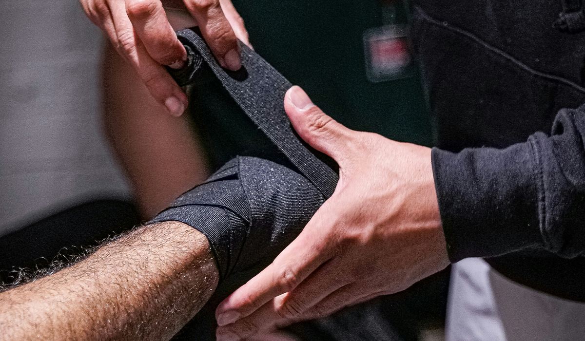 An athletic trainer wraps black athletic tape around an athlete's wrist.