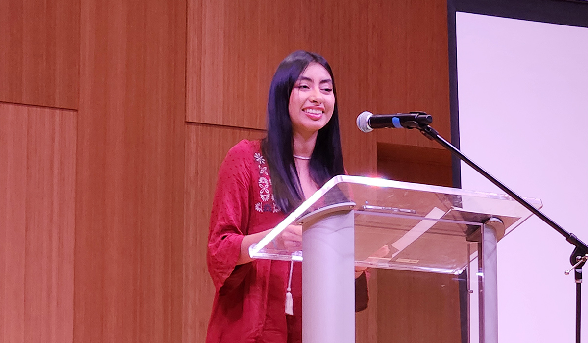 A female Latina student stands at a podium on a stage.