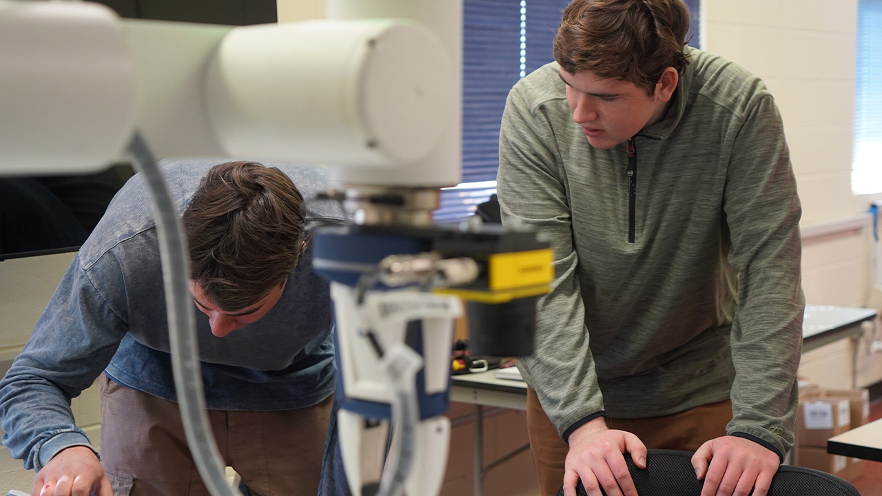 Two students work on a robotic arm.