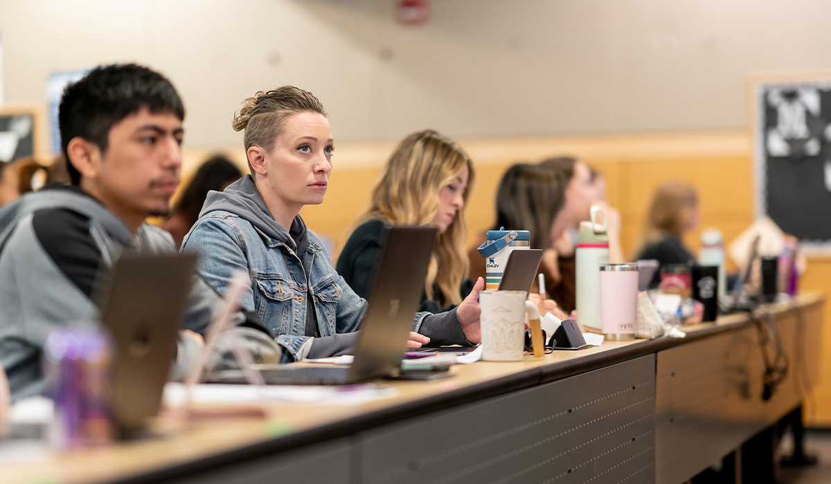A row of students seated at a long table with their laptops open.